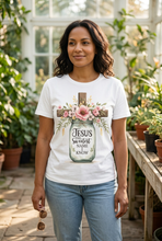 Load image into Gallery viewer, Woman wearing a white faith graphic tee with a watercolor mason jar of pink roses and a wooden cross reading Jesus the sweetest name I know, standing in a sunlit greenhouse