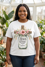 Load image into Gallery viewer, Smiling plus-size woman with long dark braids wearing a white faith graphic tee with a watercolor mason jar of pink roses and a wooden cross reading Jesus the sweetest name I know, standing in a bright conservatory
