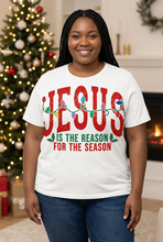 Load image into Gallery viewer, Smiling plus-size woman with long black braids wearing a white Christmas graphic tee with bold red JESUS lettering, Christmas lights, and holly, standing by a lit Christmas tree
